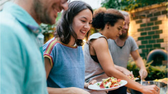 young adults outside lining up for food at a backyard barbecue